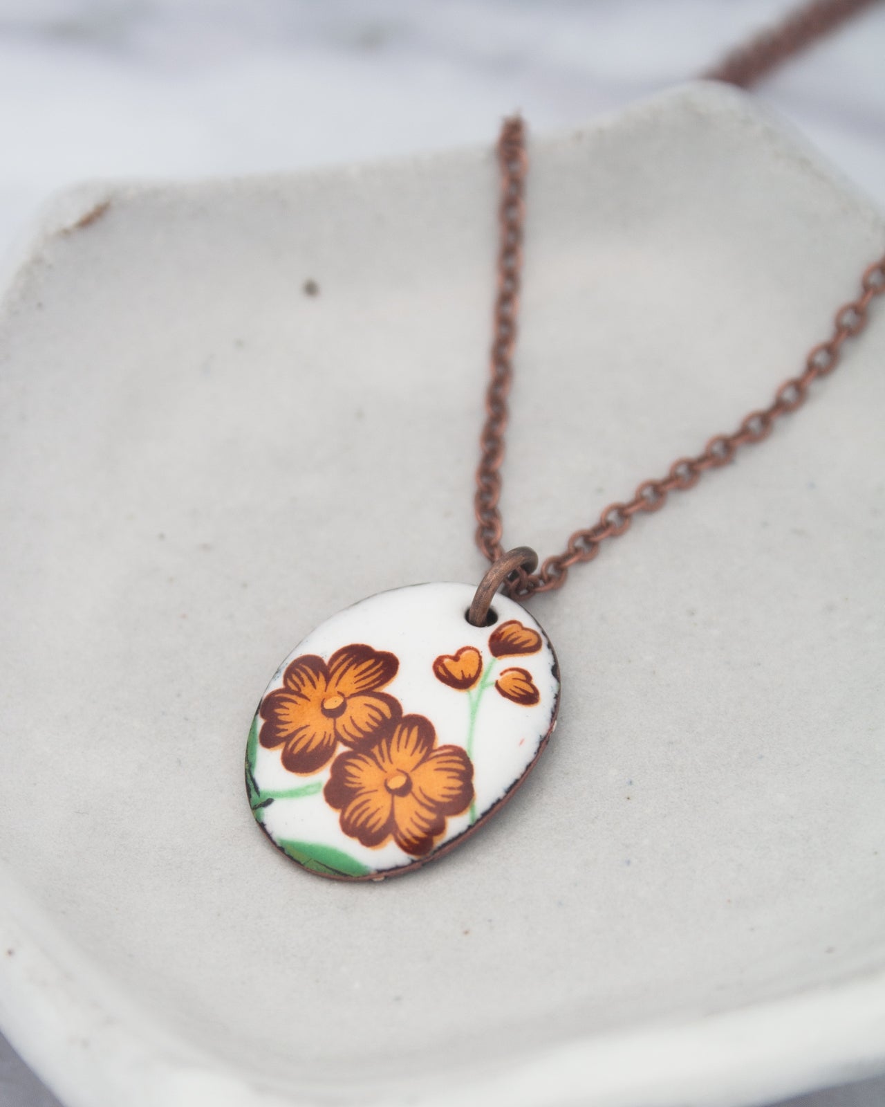 A necklace with a pendant featuring a floral design in brown and orange colors.