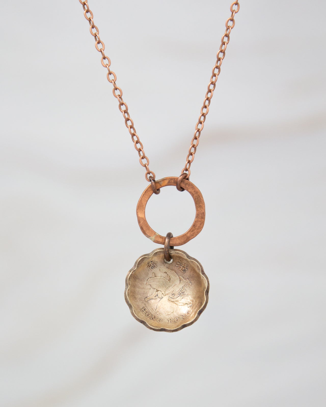 A necklace with a round metal pendant featuring an image of a bird and the text "HONG KONG" hanging from a chain.