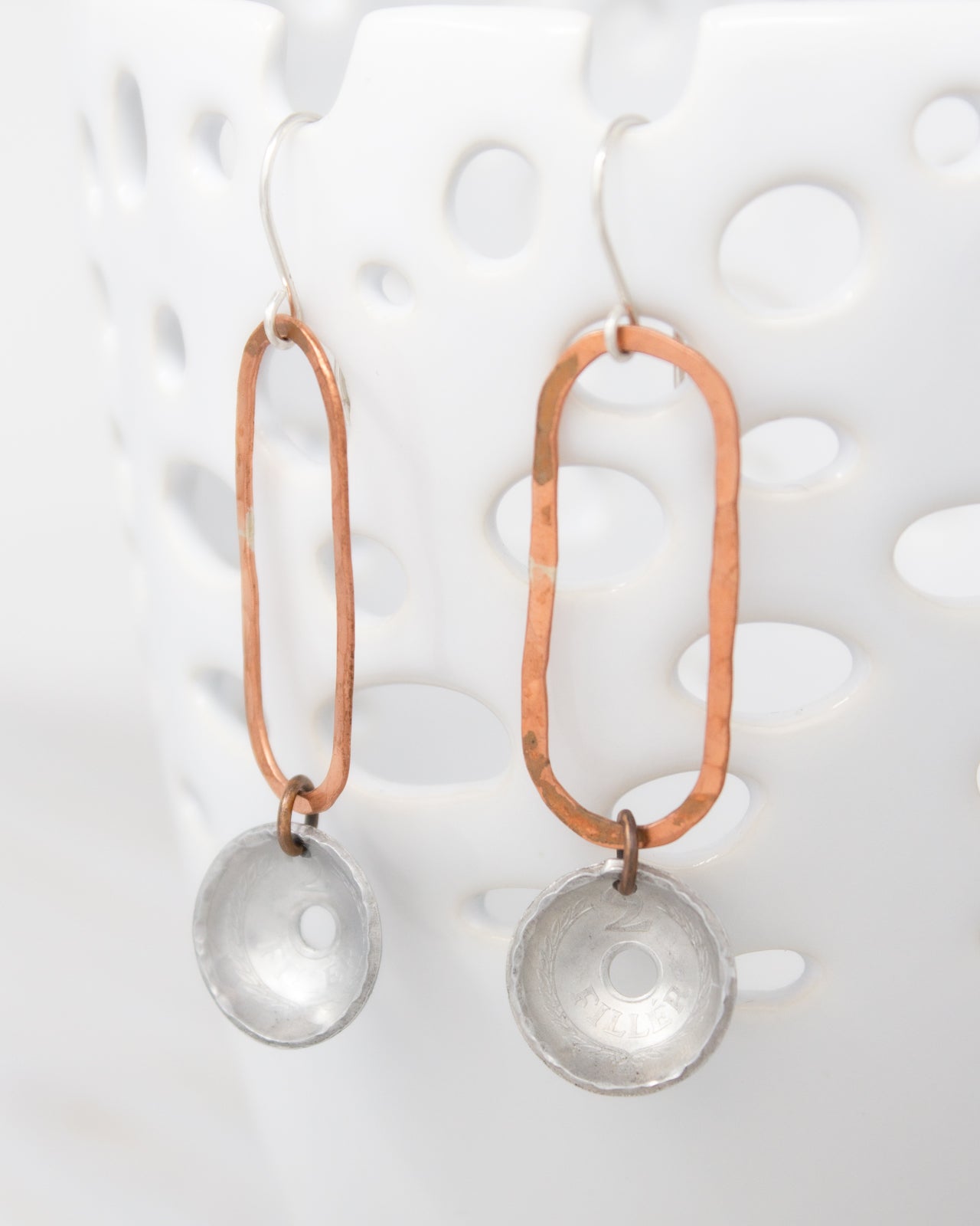 A pair of earrings with a combination of copper and silver materials, featuring a circular pendant and a metallic rod.