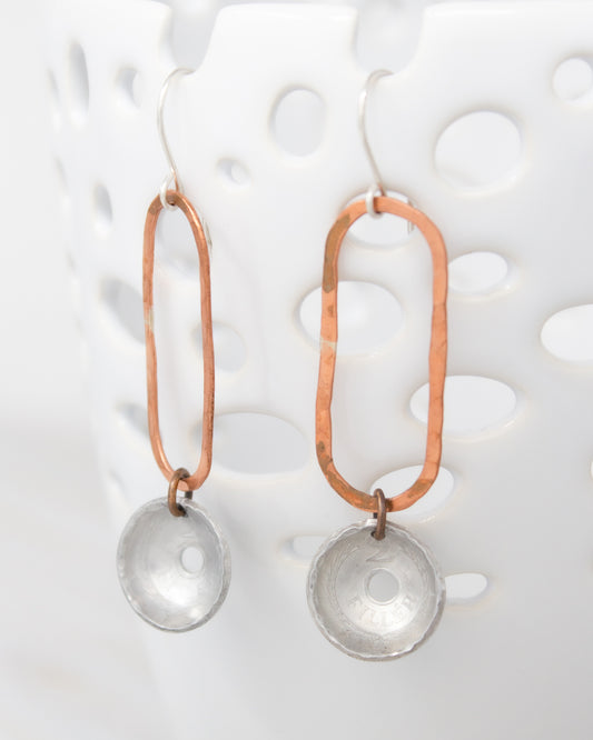A pair of earrings with a combination of copper and silver materials, featuring a circular pendant and a metallic rod.