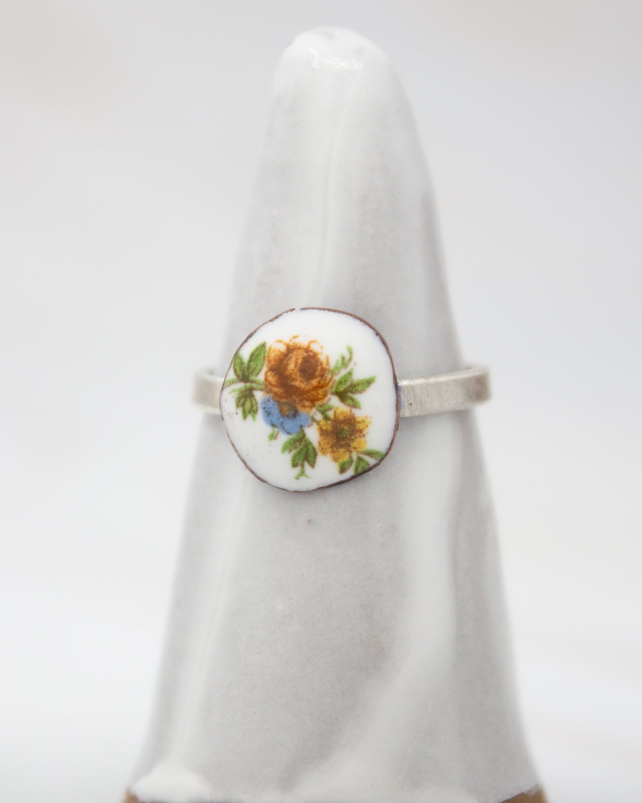 A white ceramic ring with a floral design on it, placed on a white stand.