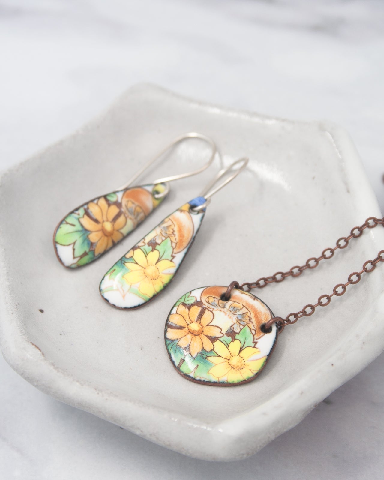 A pair of earrings and a necklace with floral designs are displayed on a white plate.
