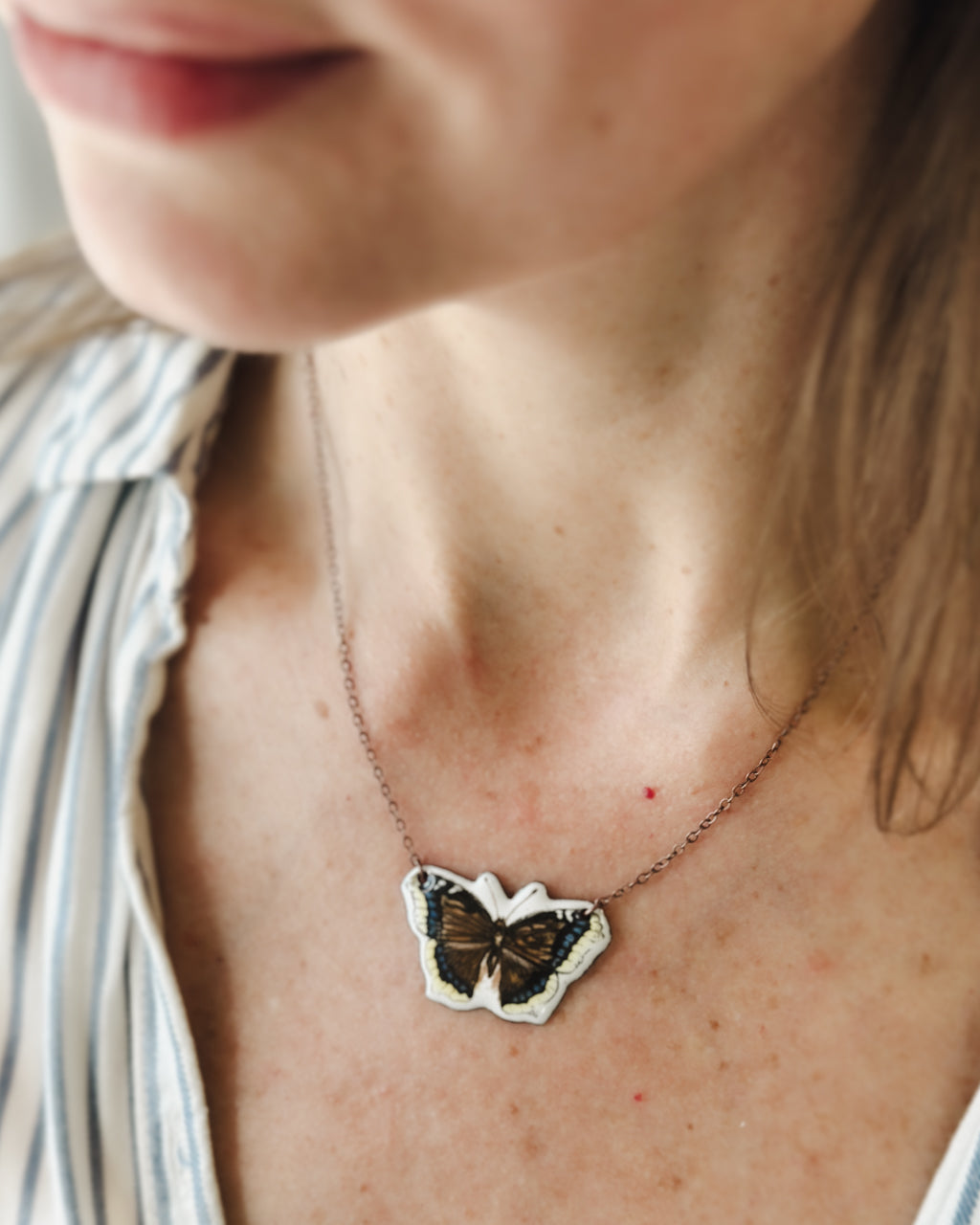 A close-up of a woman's neck and chest area, with a silver necklace featuring a butterfly pendant.