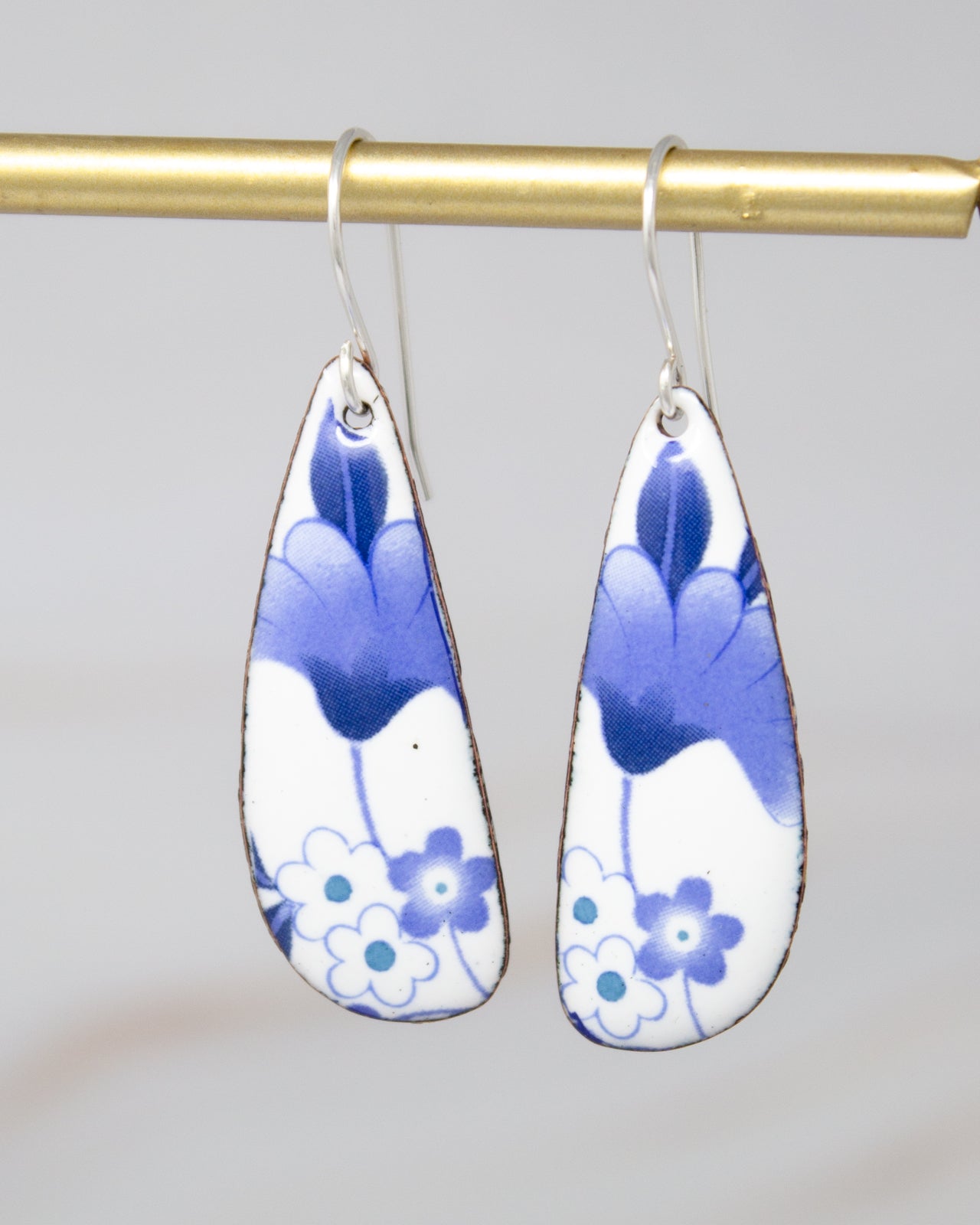 A pair of earrings with blue and white floral designs hanging from a gold bar.