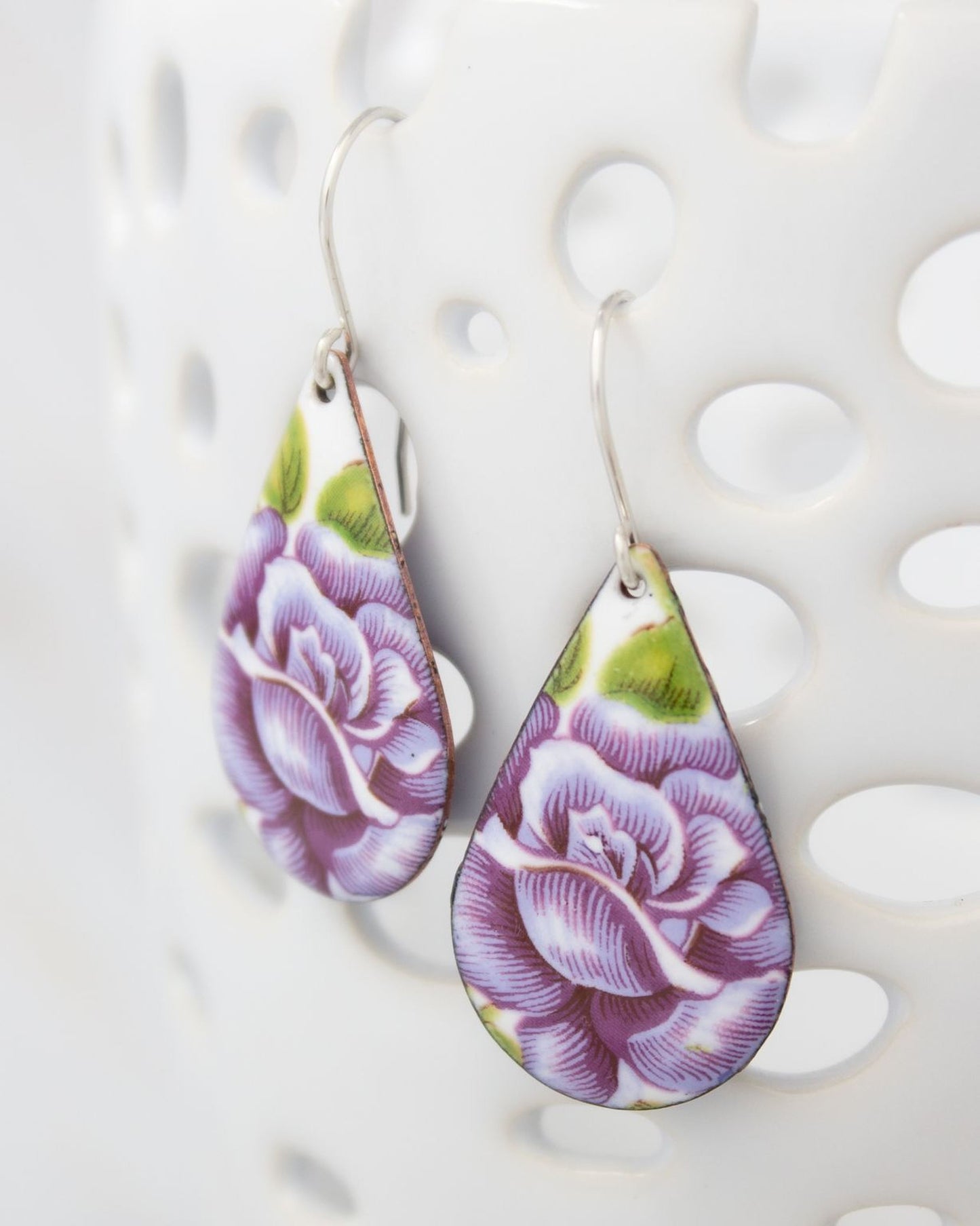A pair of earrings with a floral design, featuring purple and green colors.