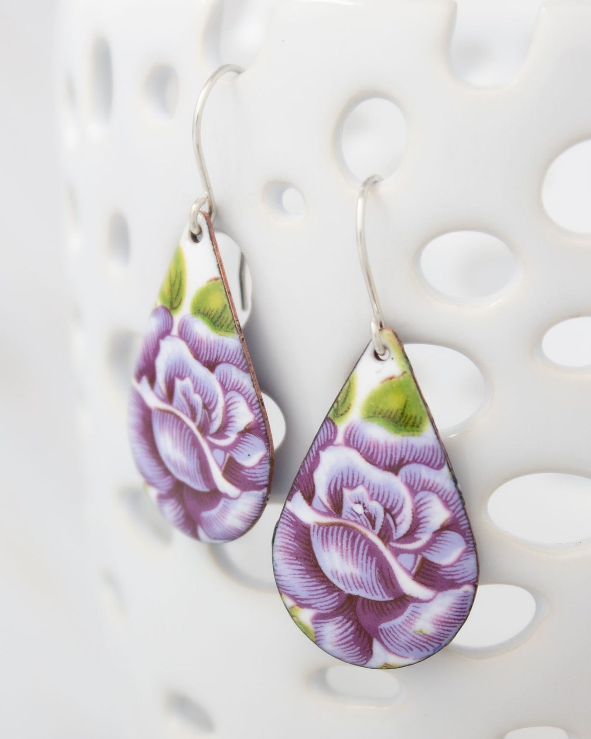 A pair of earrings with a floral design, featuring purple and green colors.