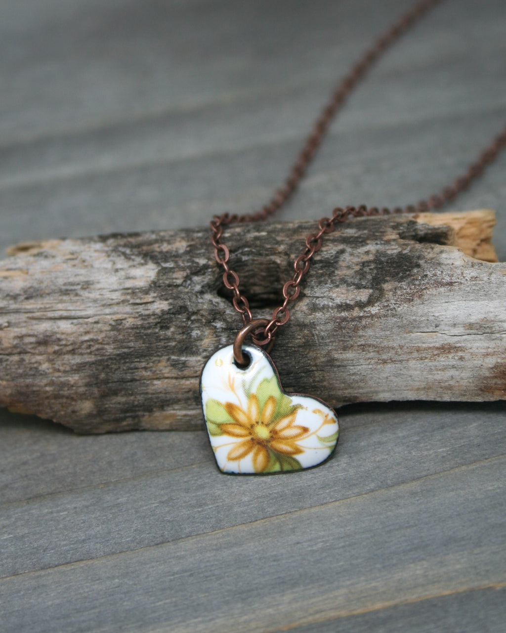 a necklace with a flower on it sitting on a piece of wood