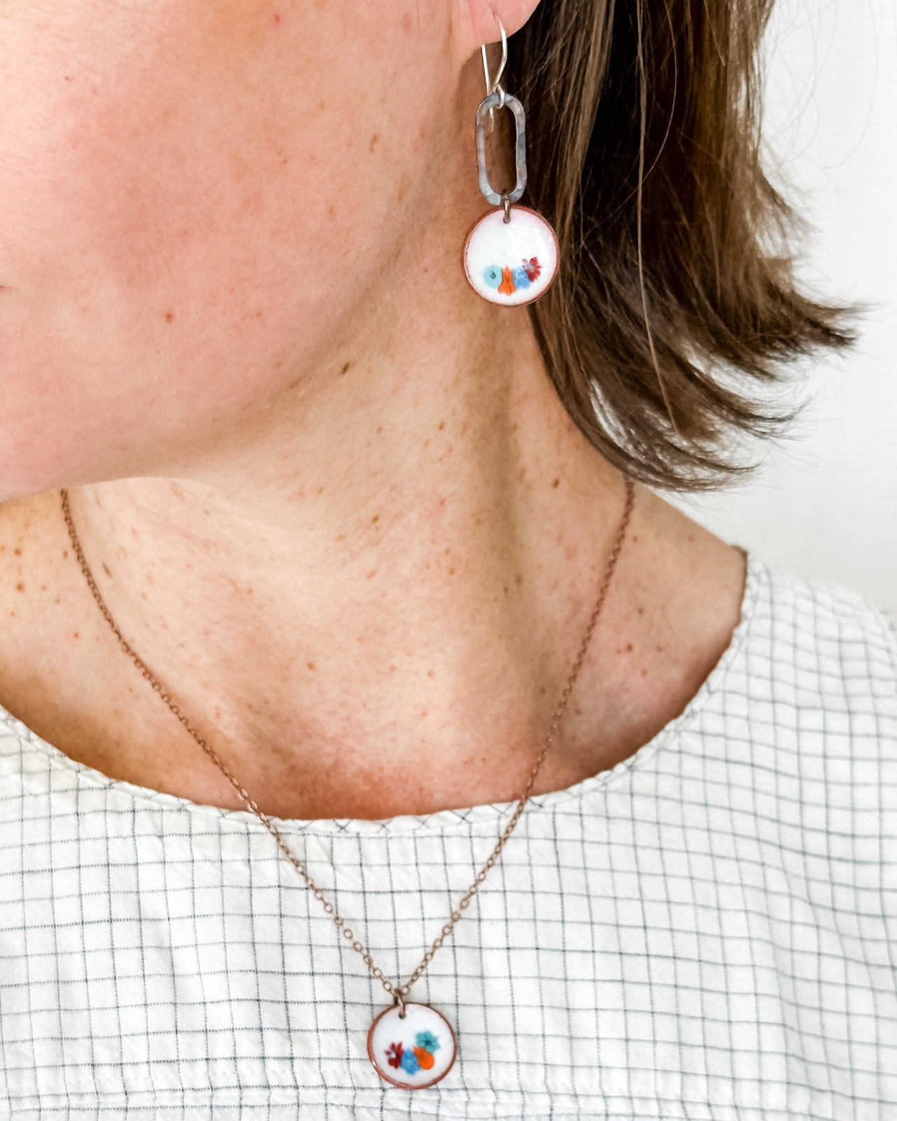 A close-up of a person's neck and chest area, featuring a necklace with a pendant and a pair of earrings.