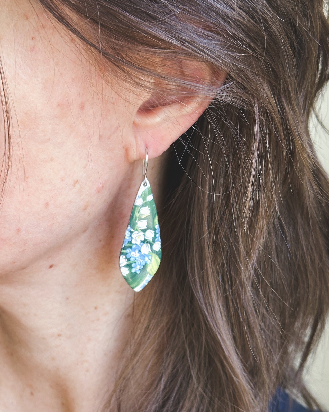 A close-up view of a person's ear wearing a green and white floral earring.