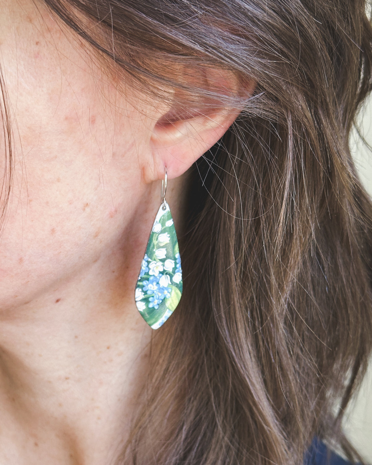 A close-up view of a person's ear wearing a green and white floral earring.