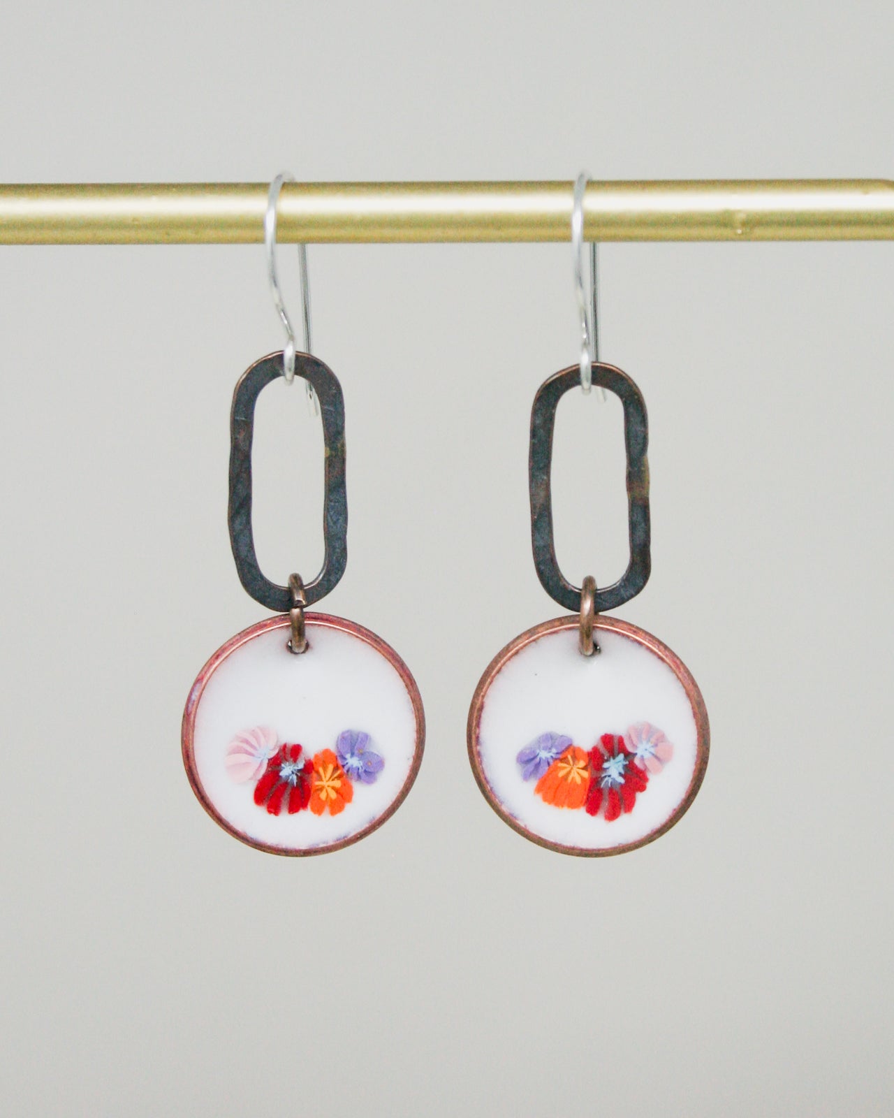 A pair of earrings with a floral design on the circular pendants, hanging from a gold-colored metal hook.