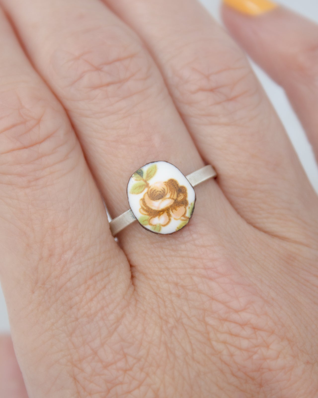 A close-up of a person's hand wearing a ring with a floral design on the finger.