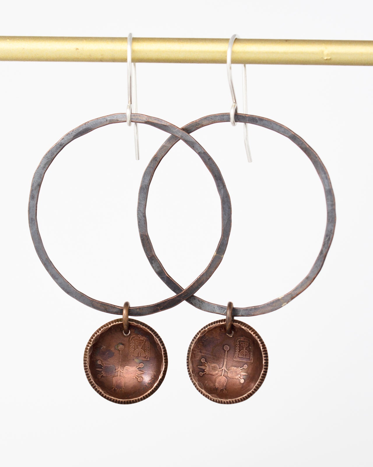 a pair of copper-colored earrings with circular metal charms hanging from a gold-colored metal bar.