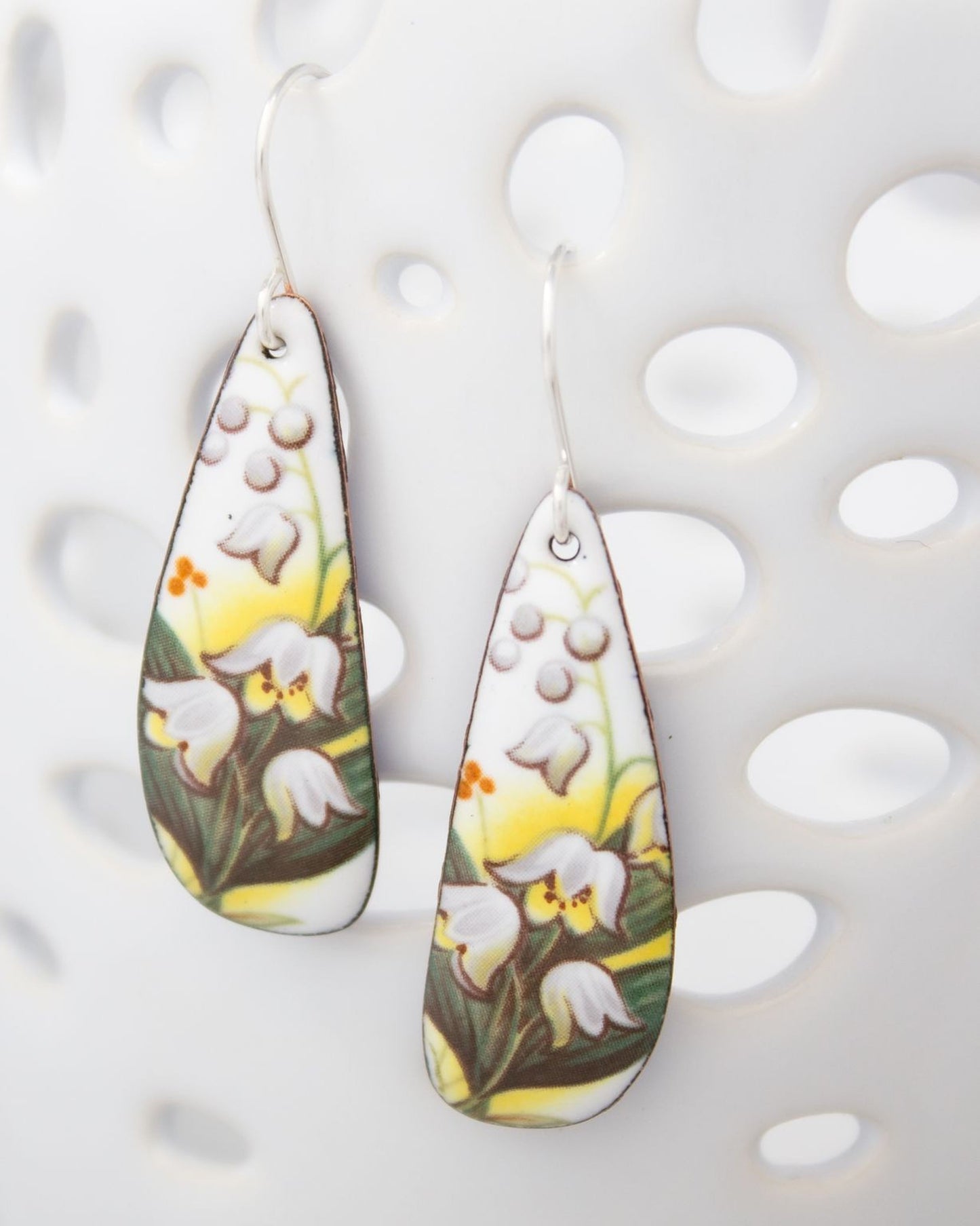 A pair of earrings with a floral design, featuring white flowers and green leaves.