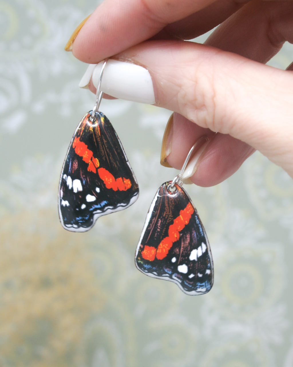 a hand holding a pair of earrings with a butterfly on it