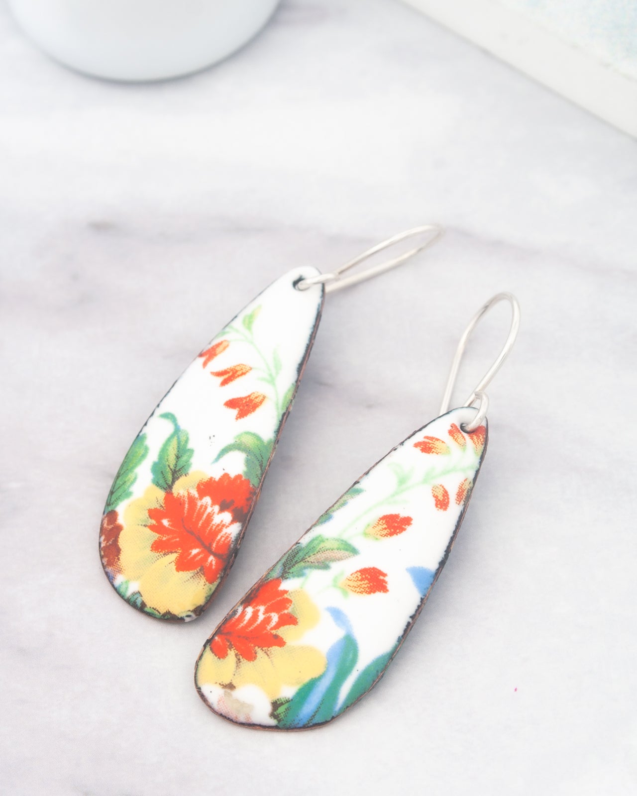 A pair of colorful earrings with floral designs on a marble surface.