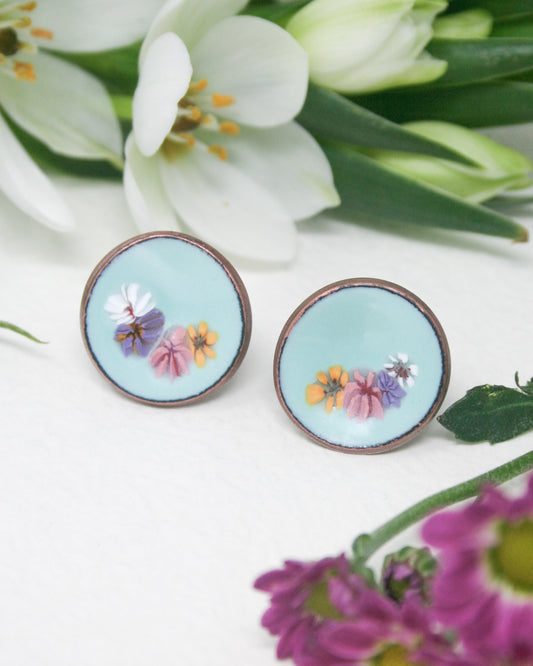a close up of a pair of earrings with flowers in the background