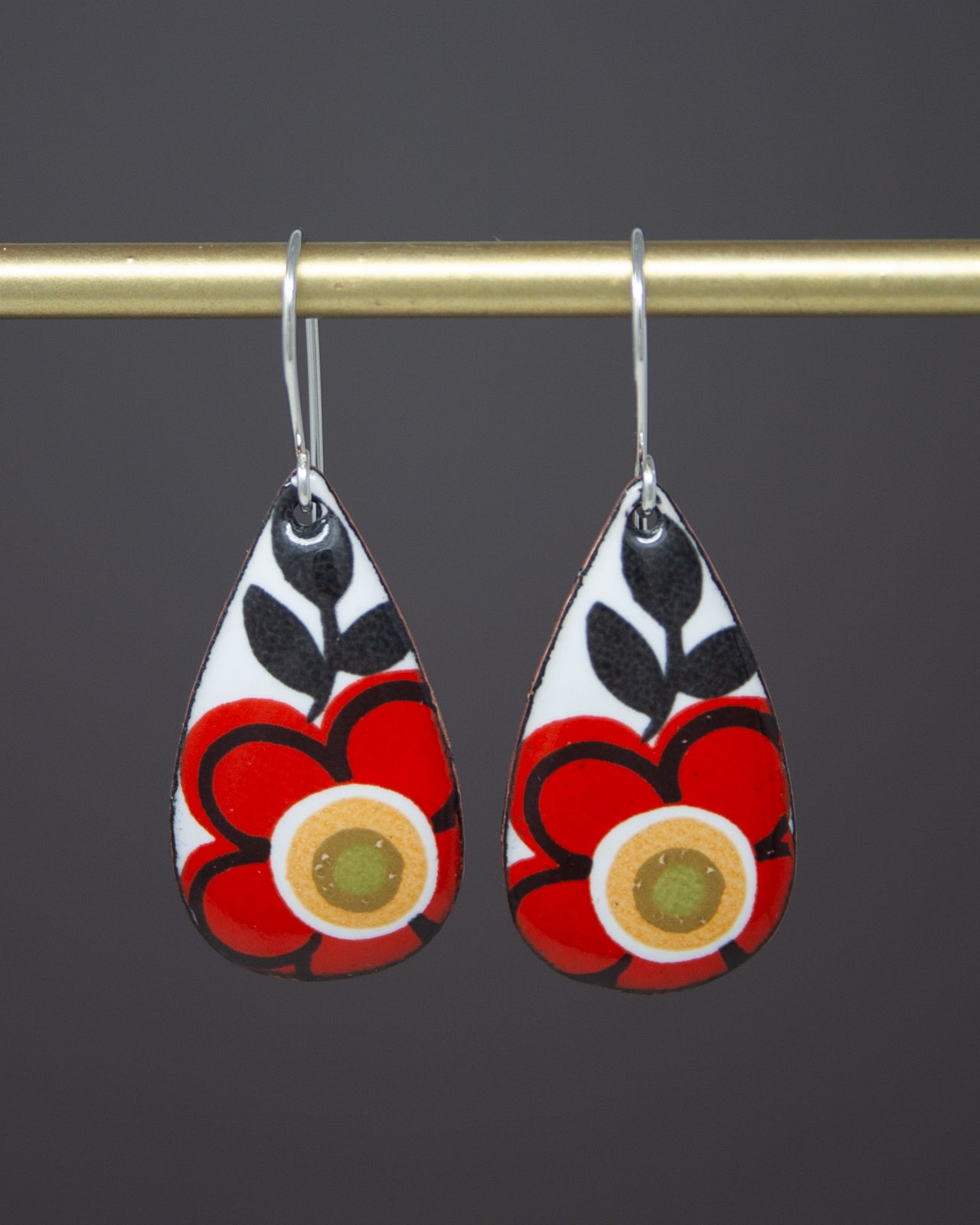 A pair of earrings with a floral design, featuring red and black flowers with a yellow center.