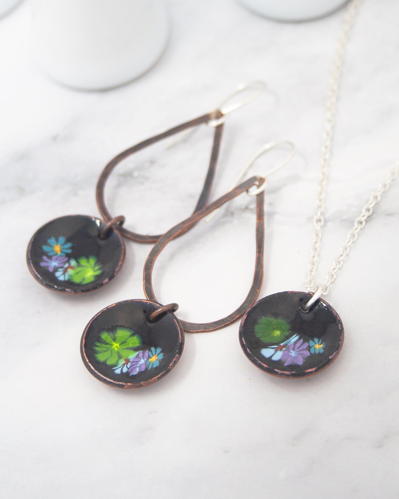 a pair of earrings and a necklace with floral designs on them, placed on a marble surface.