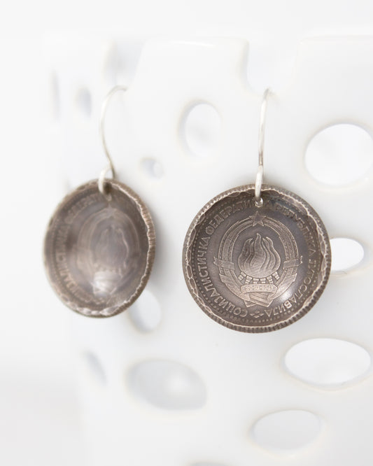 a pair of silver earrings with a round metal design featuring a coat of arms or emblem.