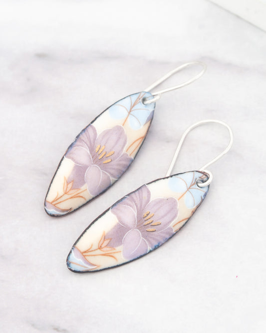 A pair of earrings with a floral design, featuring purple and white flowers against a light background.