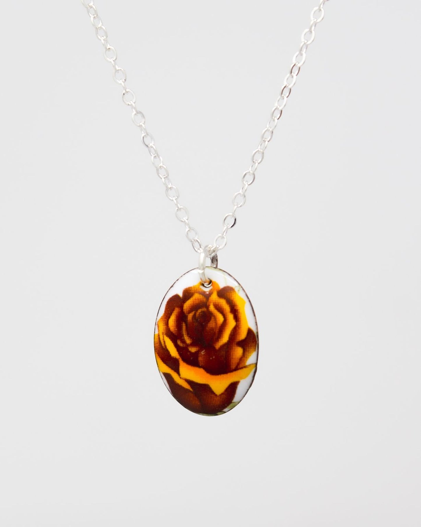A silver necklace with a round pendant featuring a flower design in shades of brown and yellow.