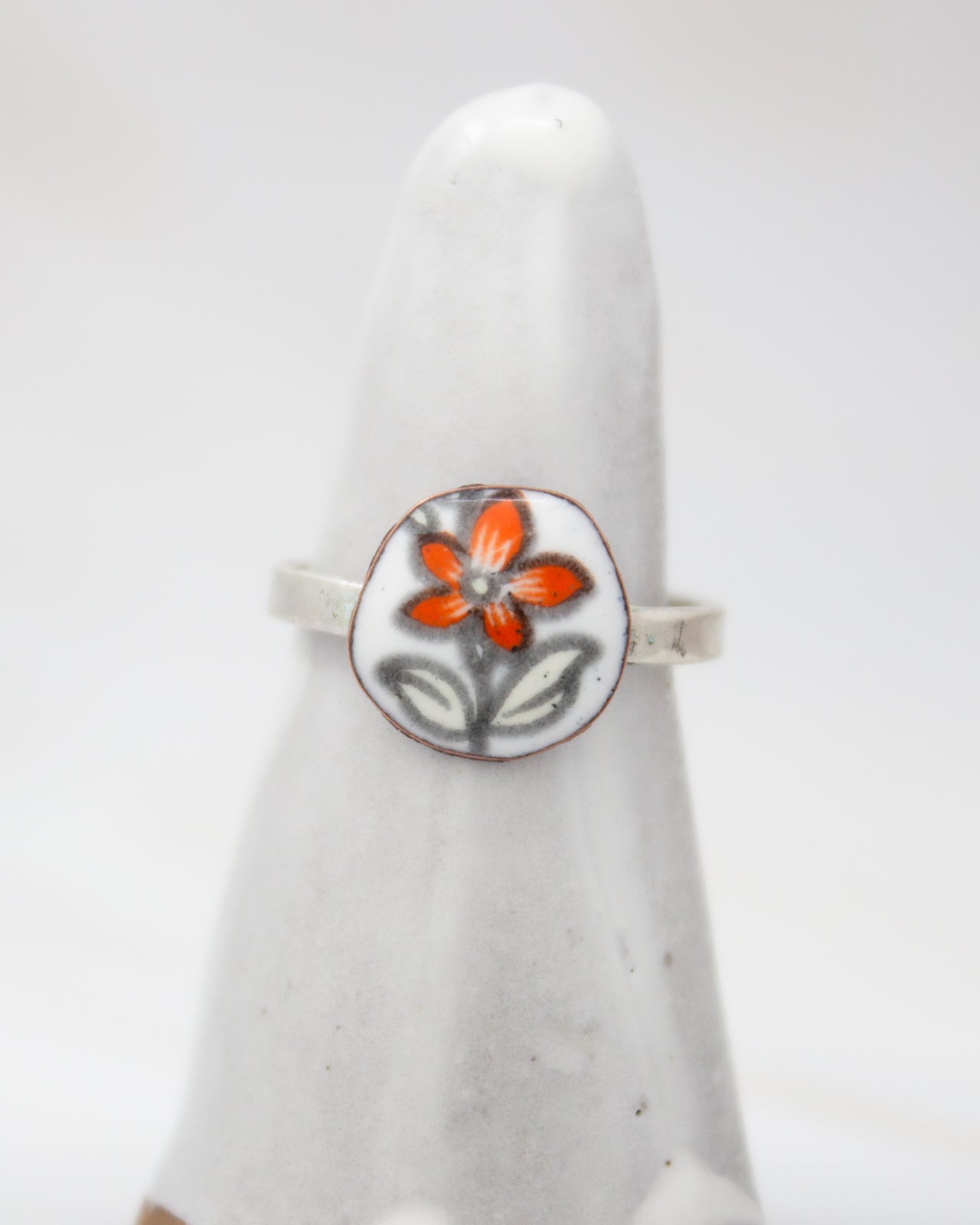 A white ceramic ring with a floral design on it, featuring a large orange flower and smaller white flowers.
