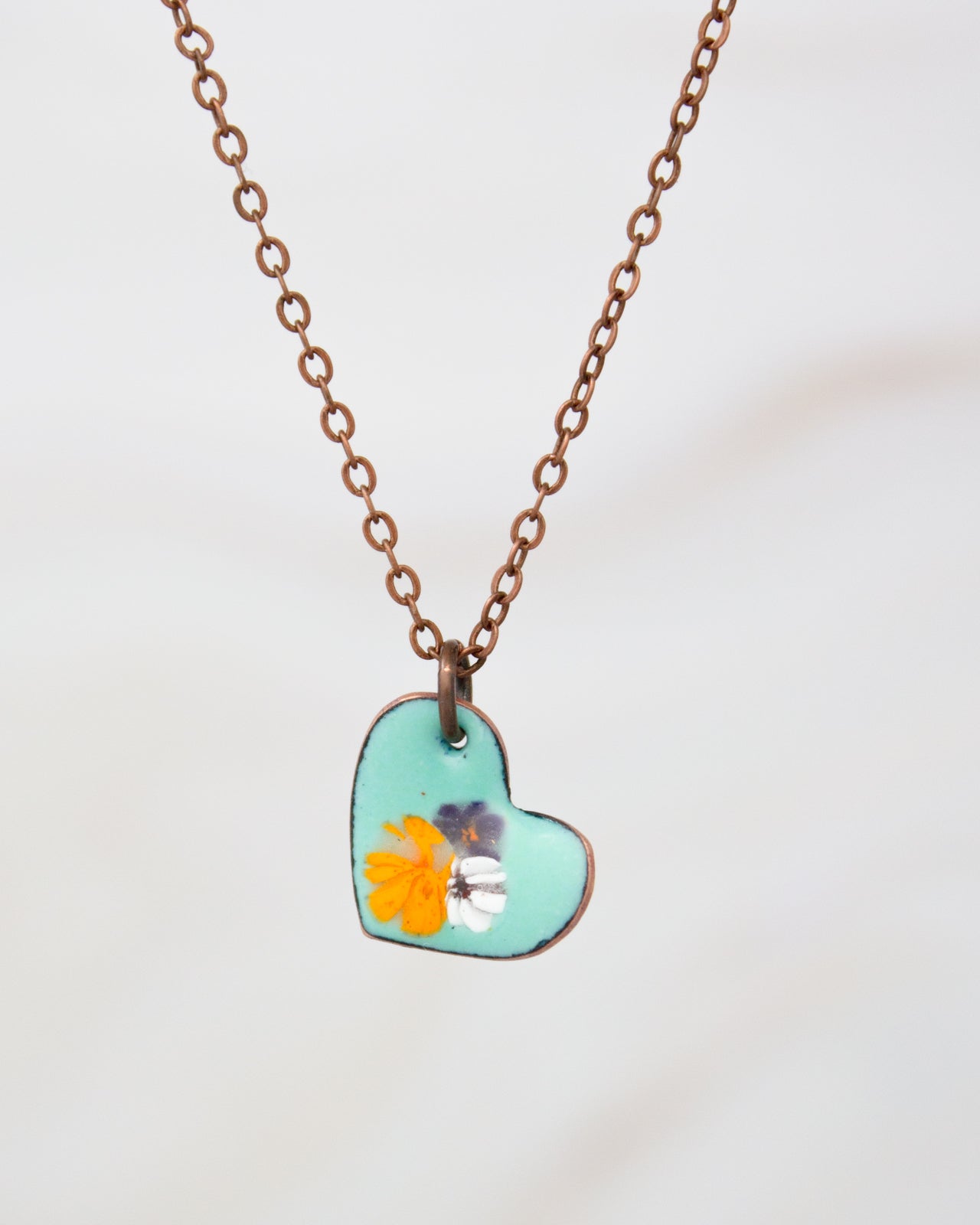 A necklace with a heart-shaped pendant featuring a floral design in turquoise and orange colors.