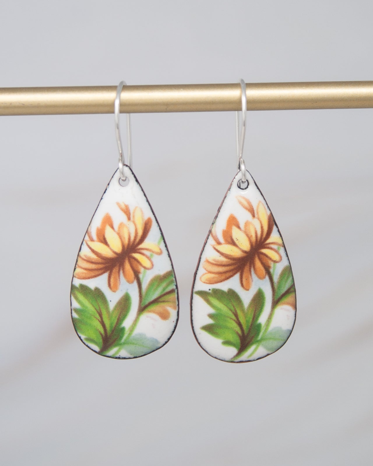 A pair of earrings with a floral design, featuring a yellow flower and green leaves.