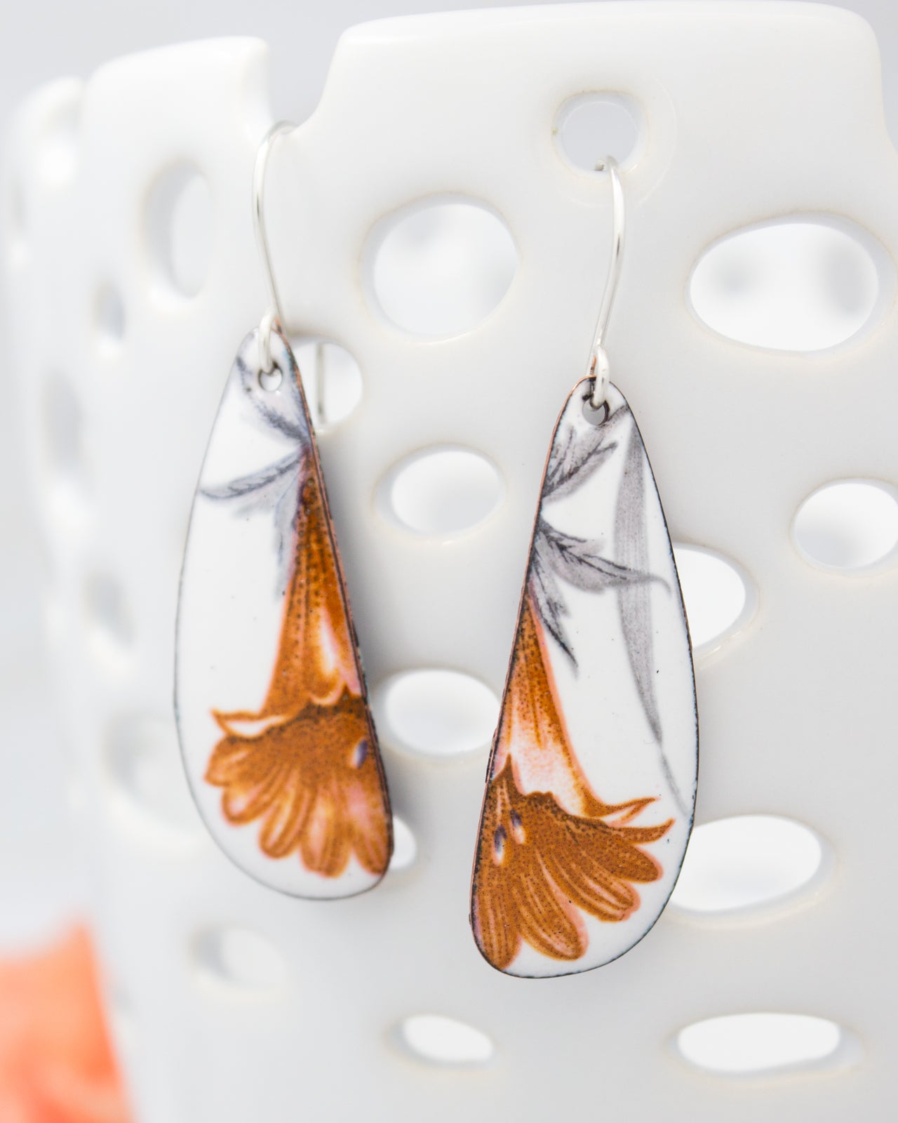 A pair of earrings with a floral design, featuring orange and white colors.