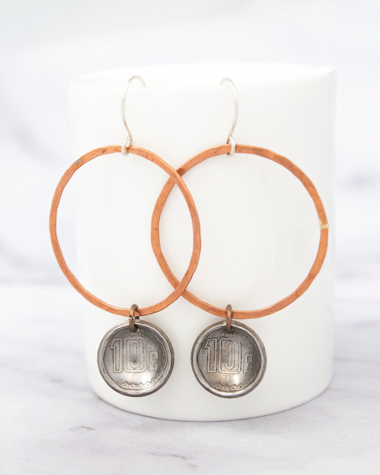 A pair of earrings with a copper-colored metal frame and silver-colored metal charms hanging from them.