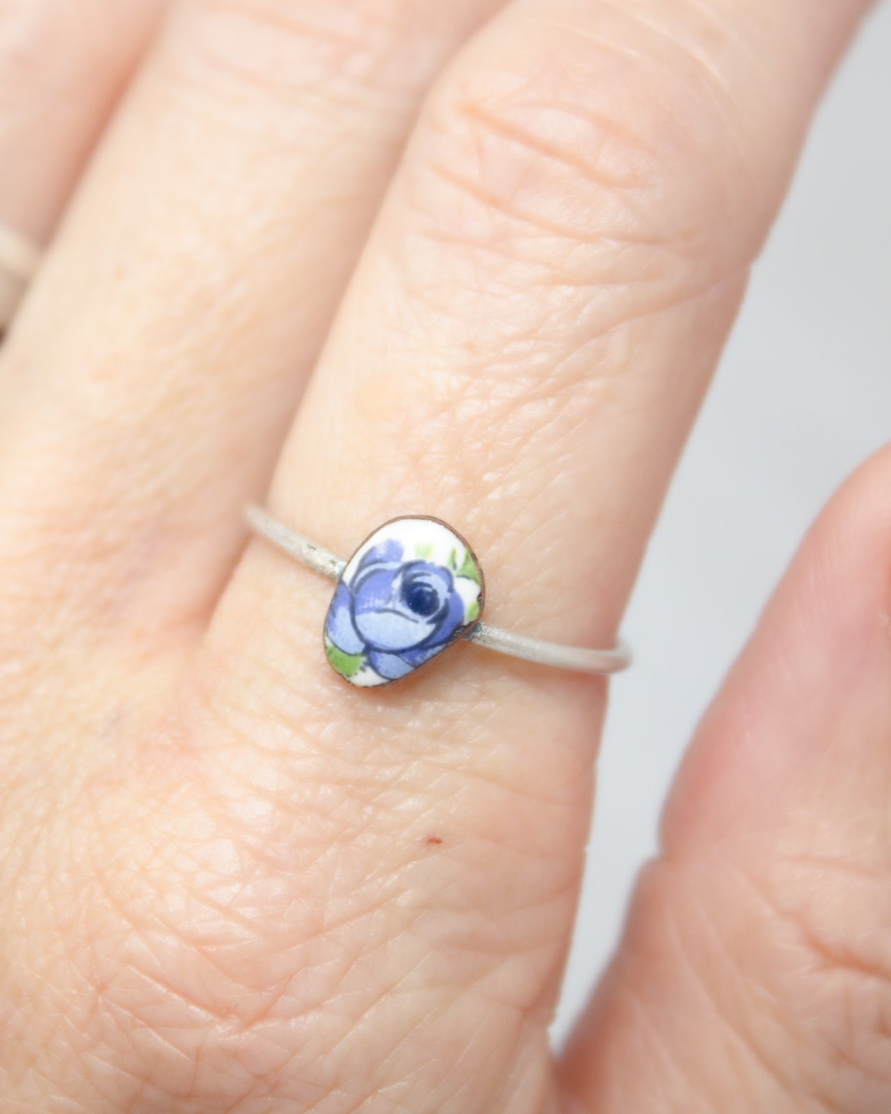 A close-up of a person's hand wearing a ring with a blue flower design.