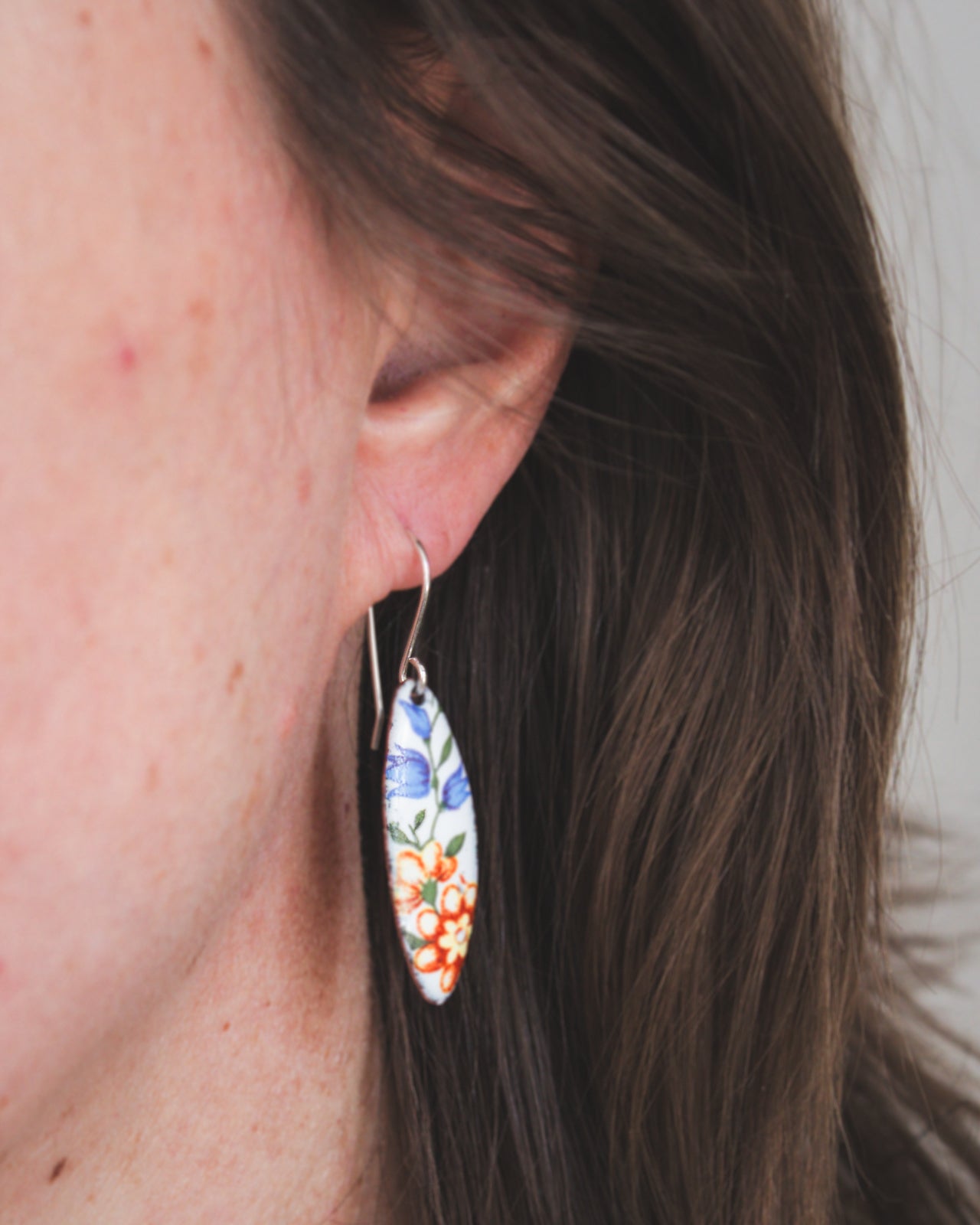 A close-up view of a person's ear wearing a pair of earrings with a floral design.