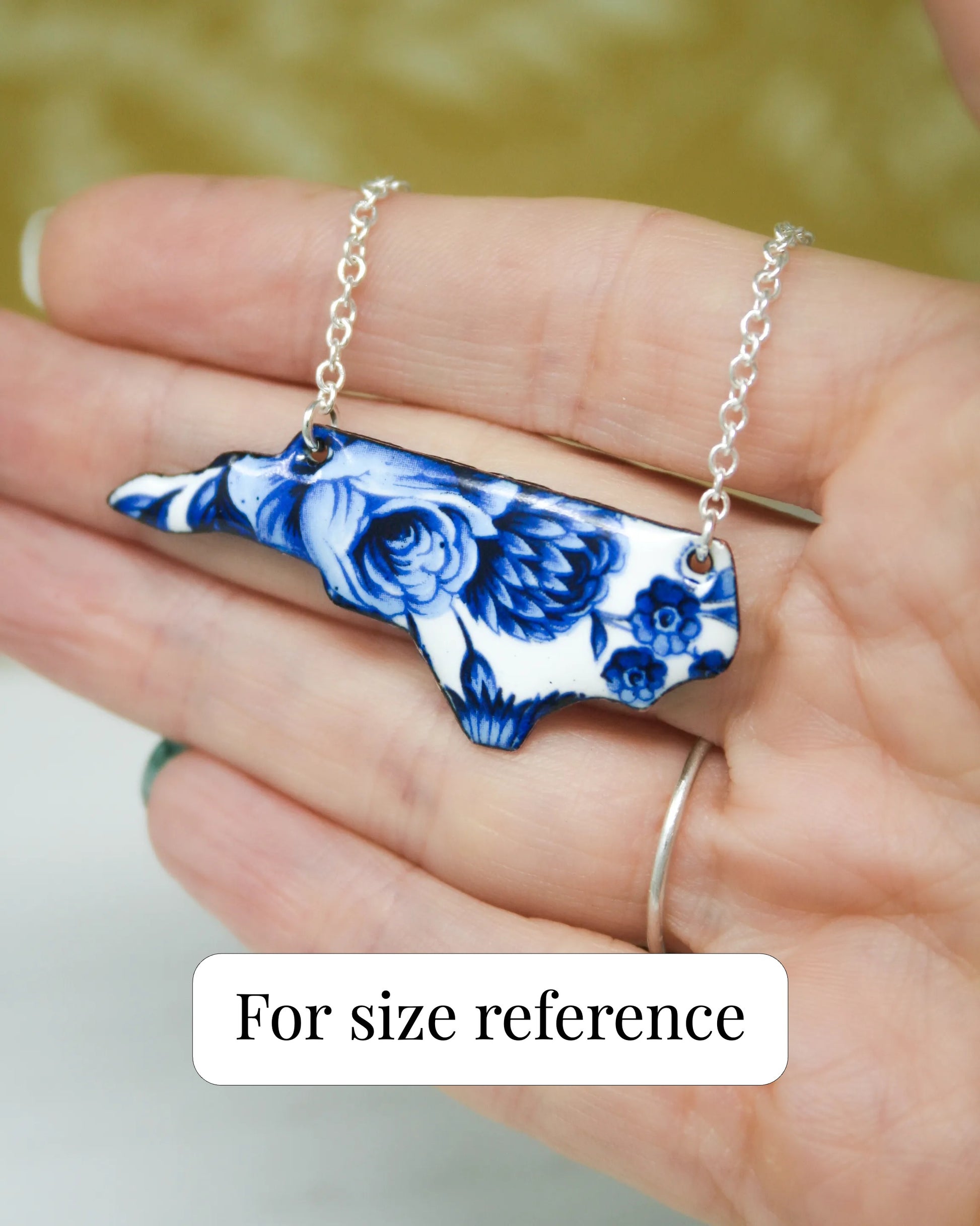 A hand holding a necklace with a blue and white floral design.