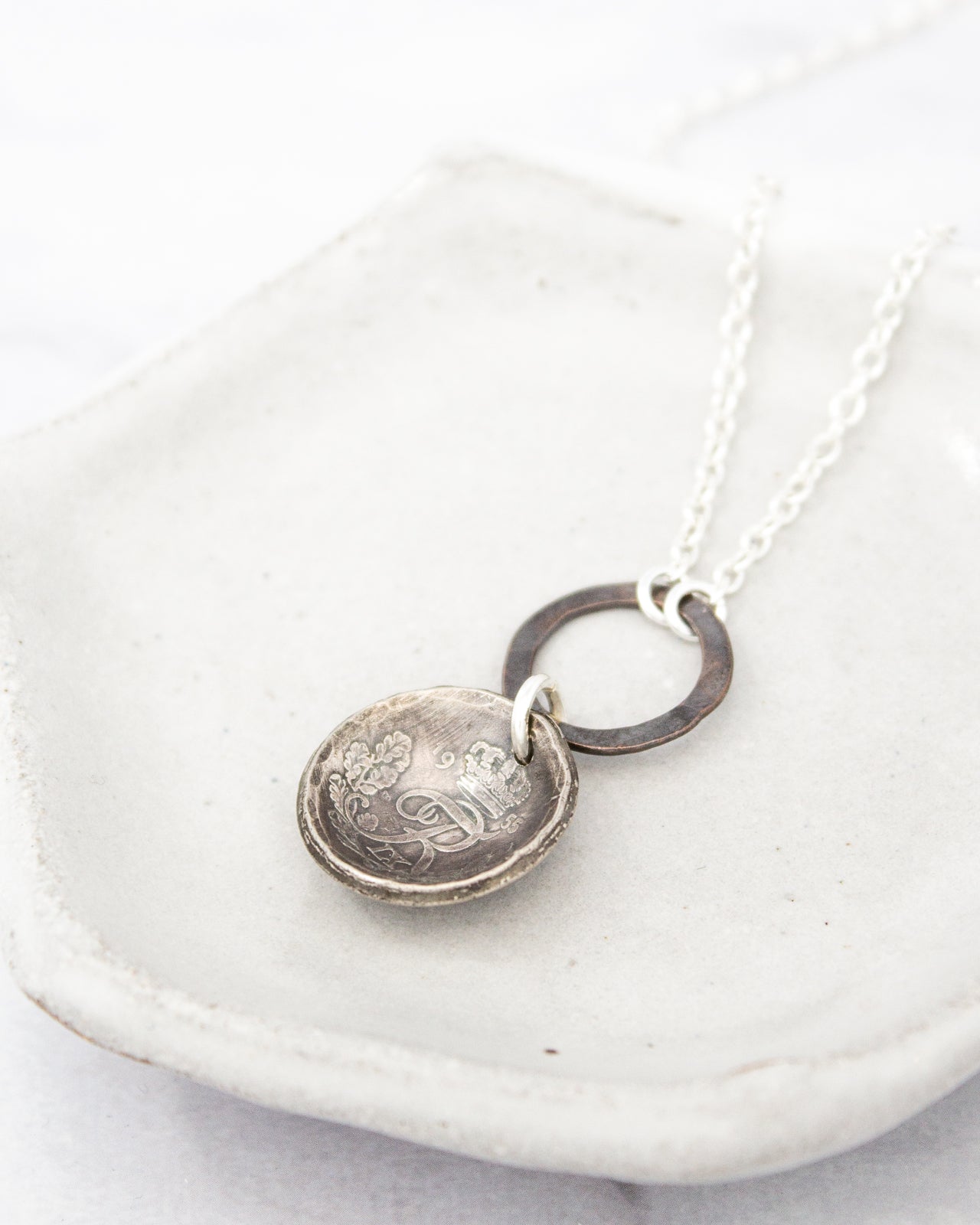 A silver necklace with a round pendant featuring an engraved design, resting on a white surface.