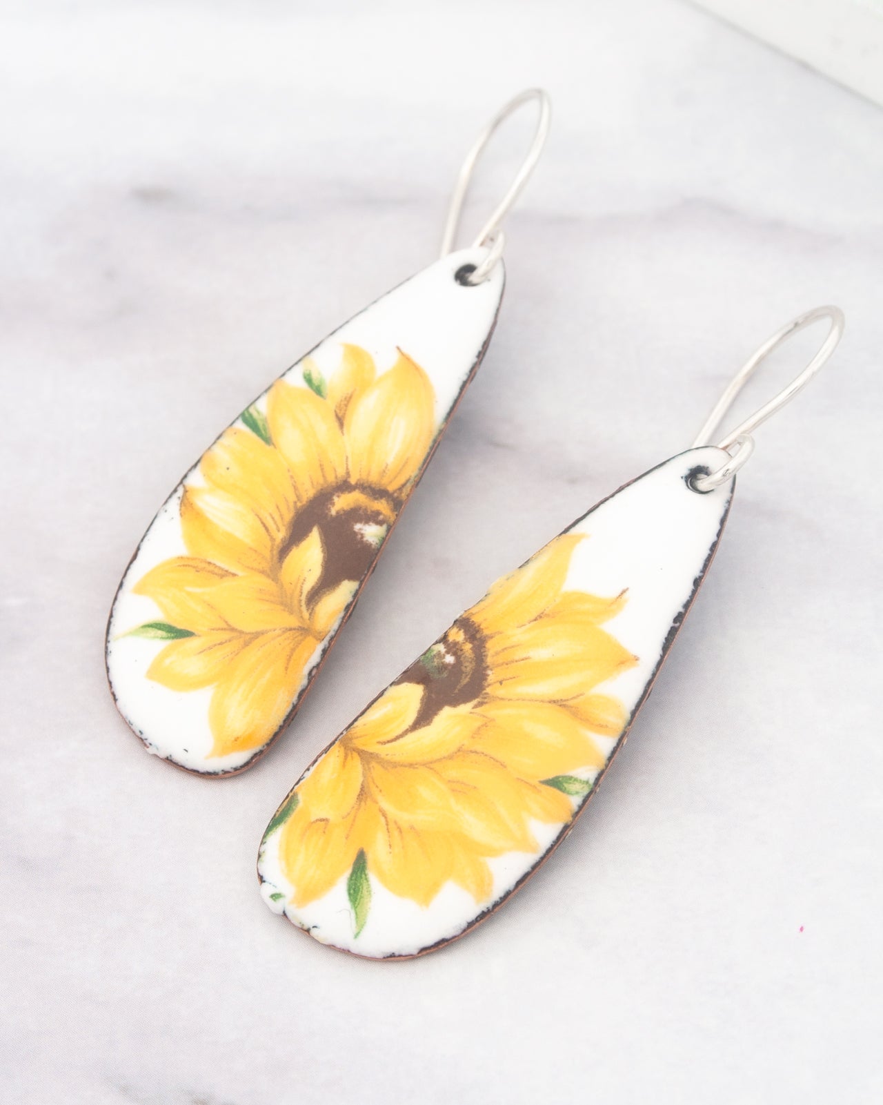A pair of white earrings with yellow sunflower designs on them.