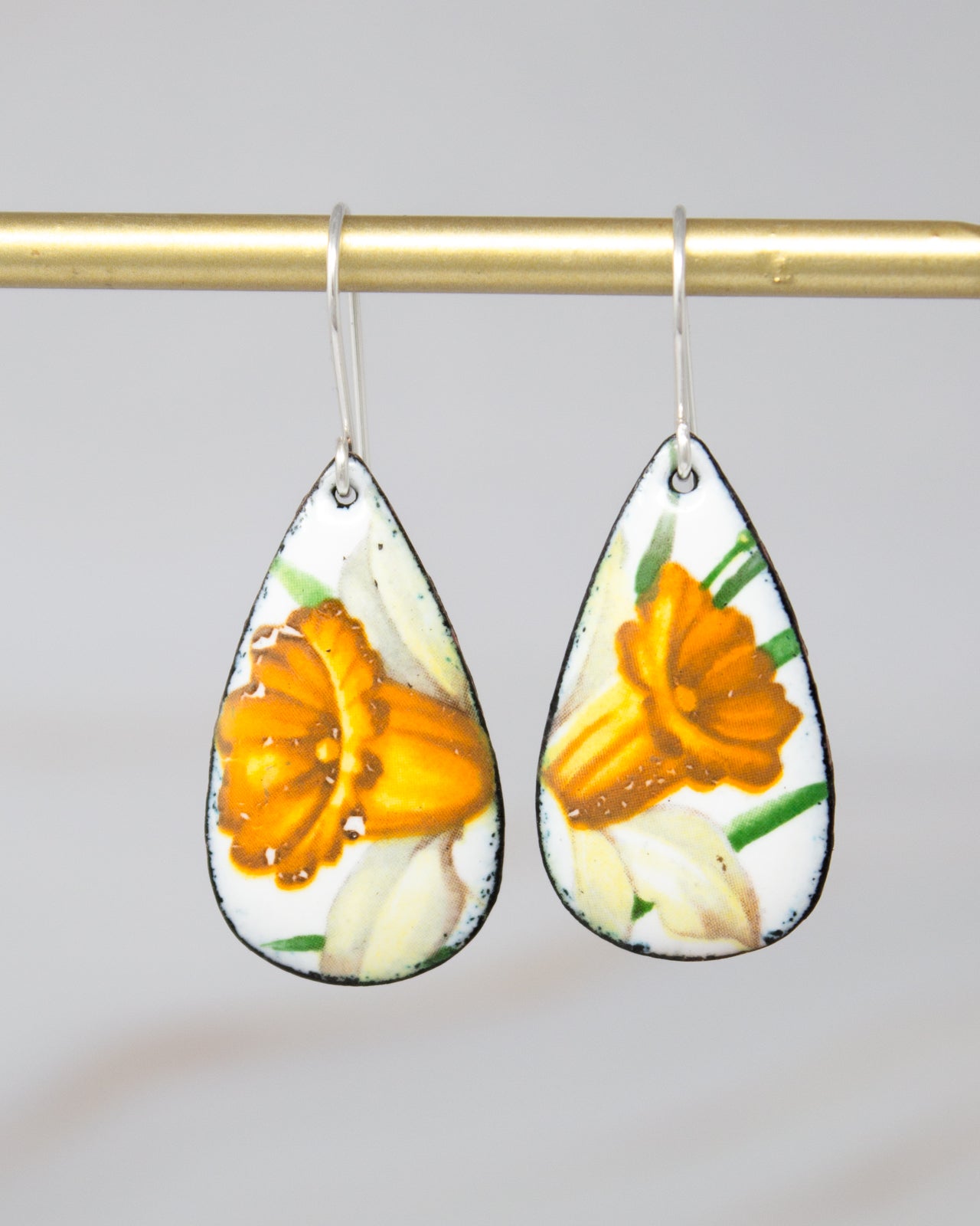 A pair of earrings with a floral design, featuring two yellow flowers on a white background.