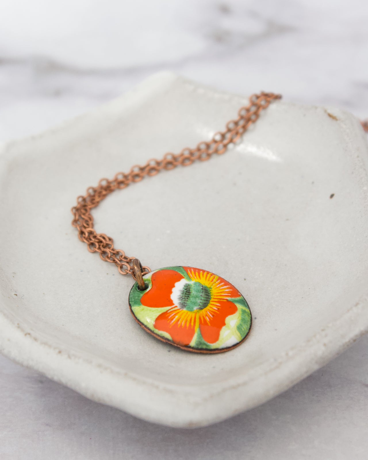 A necklace with a pendant featuring a colorful floral design is displayed on a white ceramic dish.
