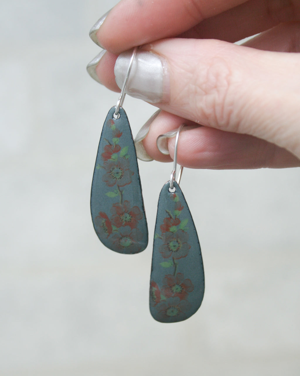 A hand holding a pair of earrings with a floral design.