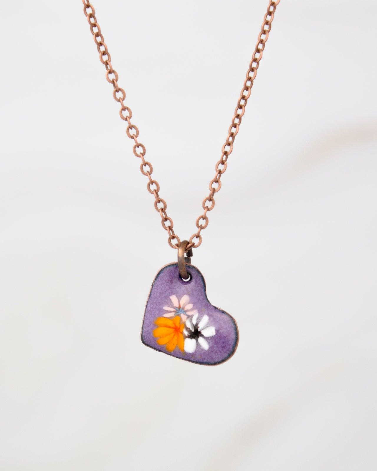 A heart-shaped pendant necklace with a purple background and colorful flowers.