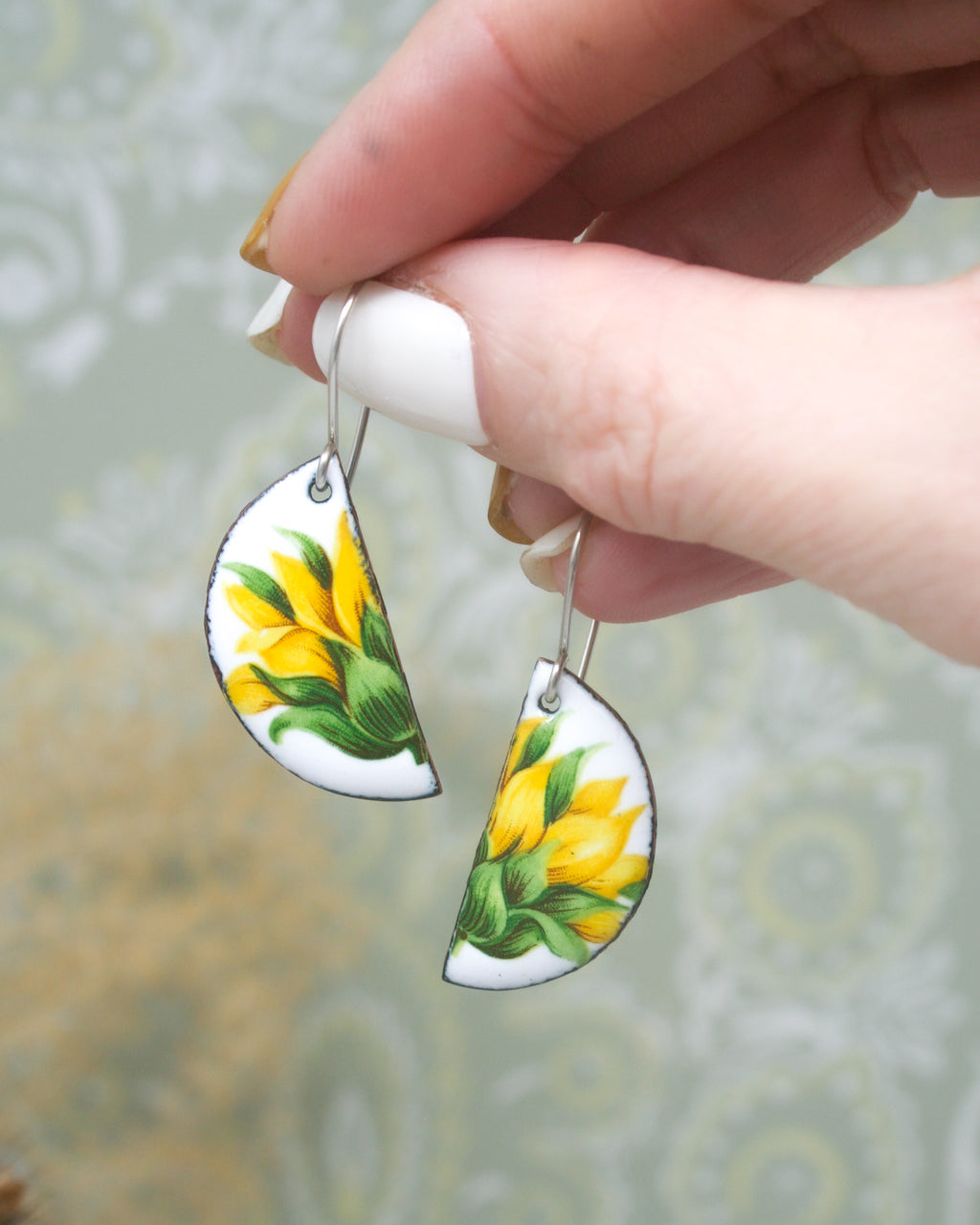 A hand holding a pair of earrings with yellow flower designs.