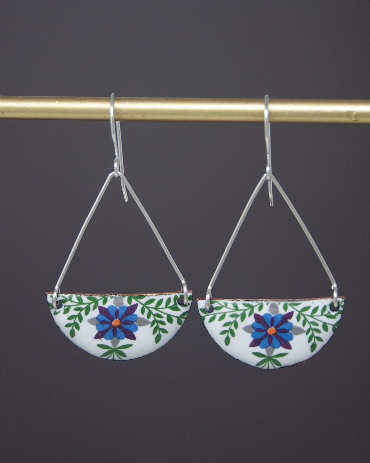 A pair of earrings with a floral design hanging from a gold-colored metal hook.