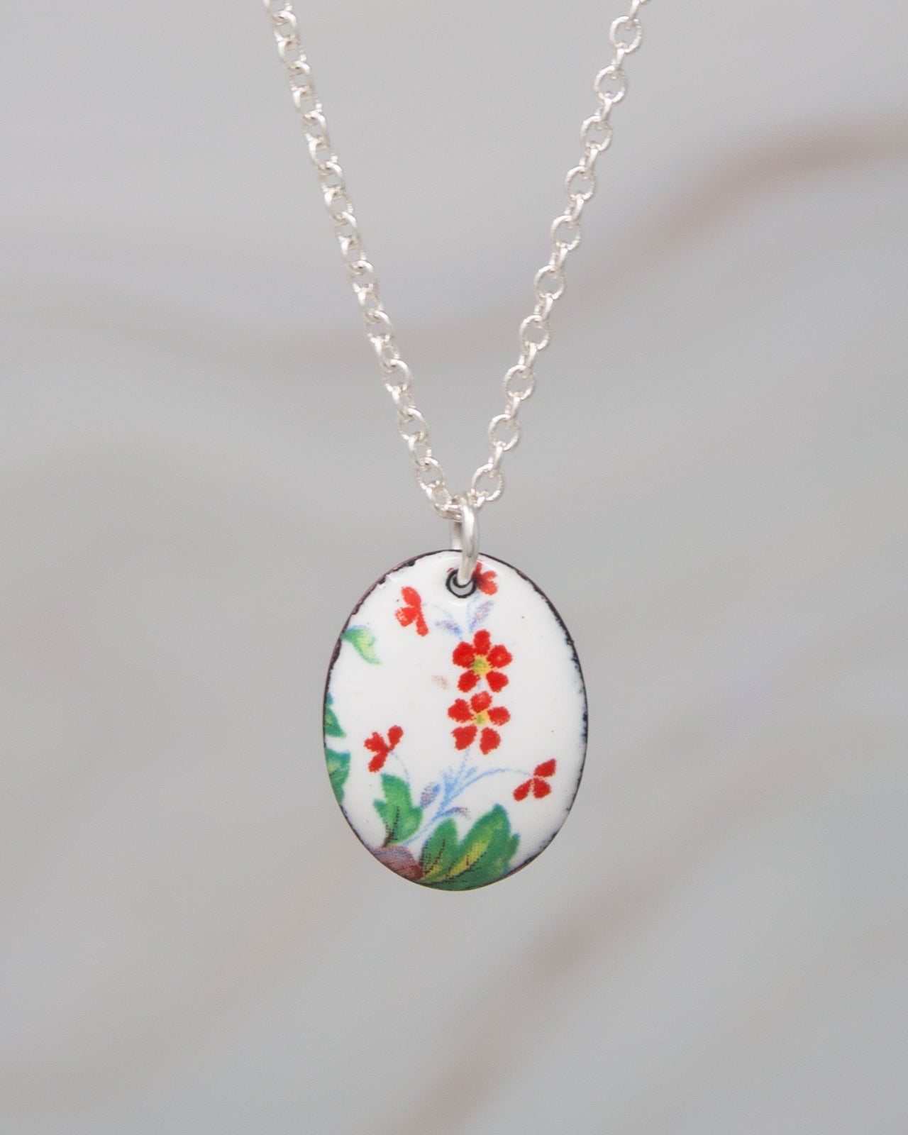 A silver necklace with a pendant featuring a floral design in red and green colors.
