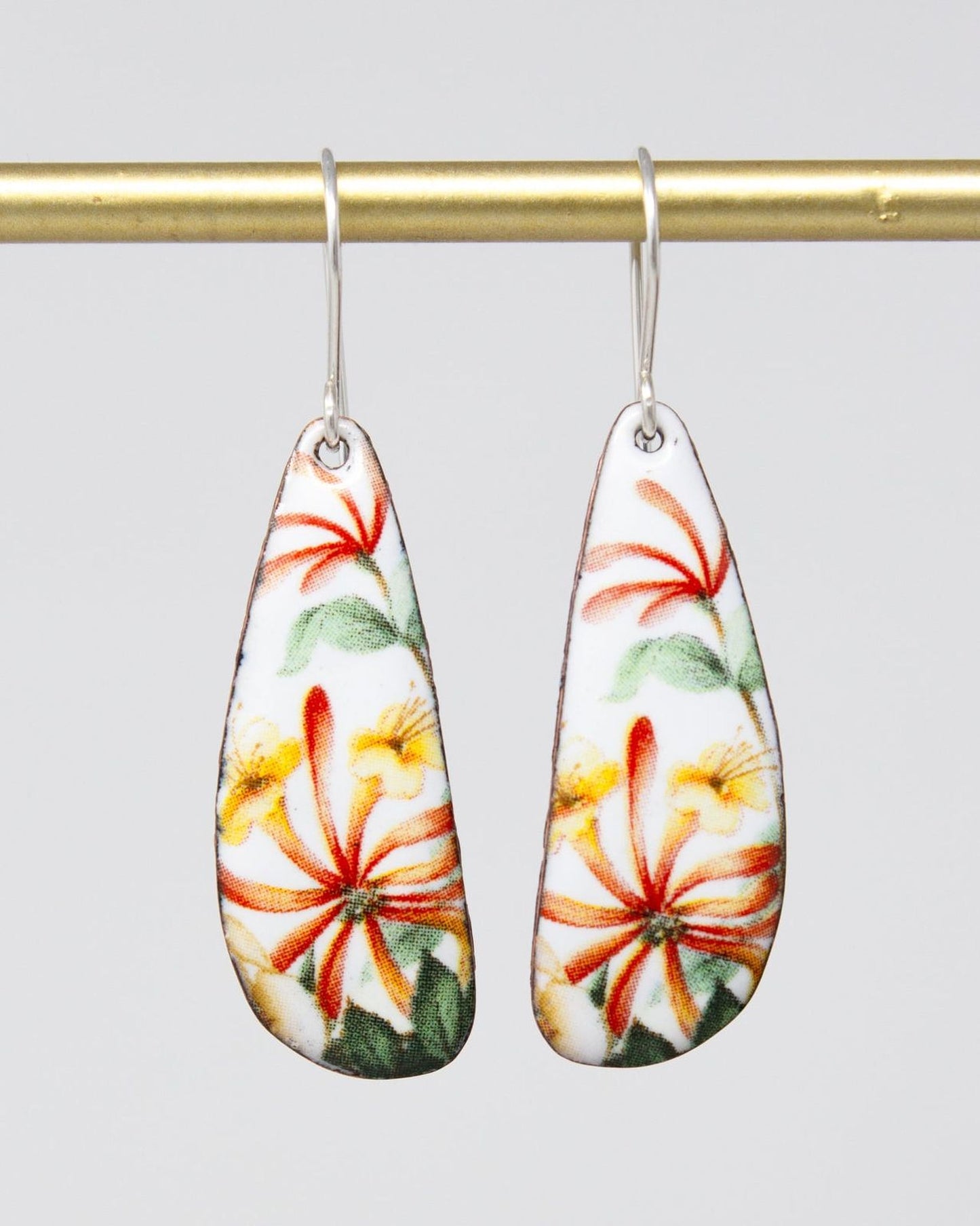 A pair of earrings with a floral design, featuring red, yellow, and green flowers on a white background.