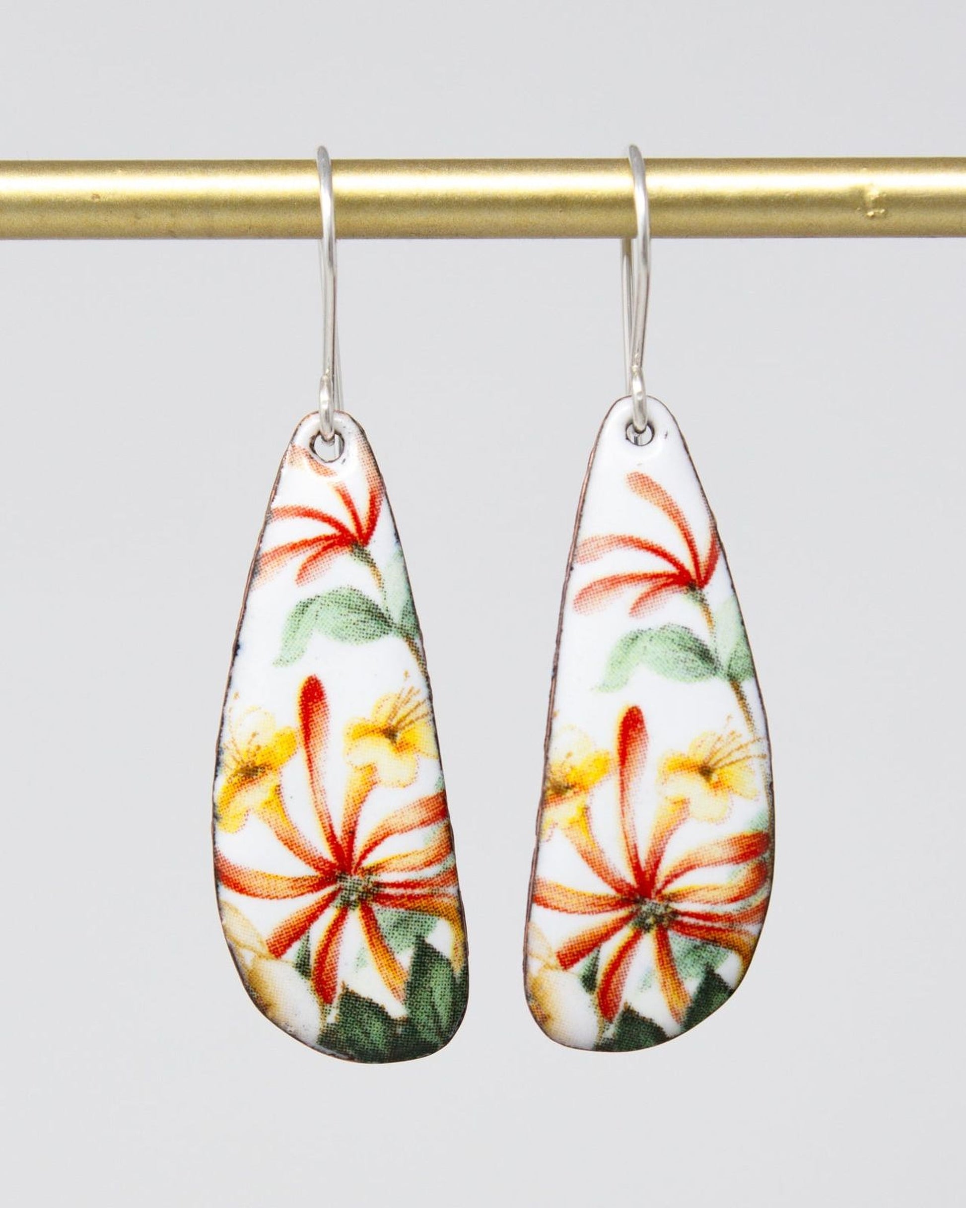 A pair of earrings with a floral design, featuring red, yellow, and green flowers on a white background.