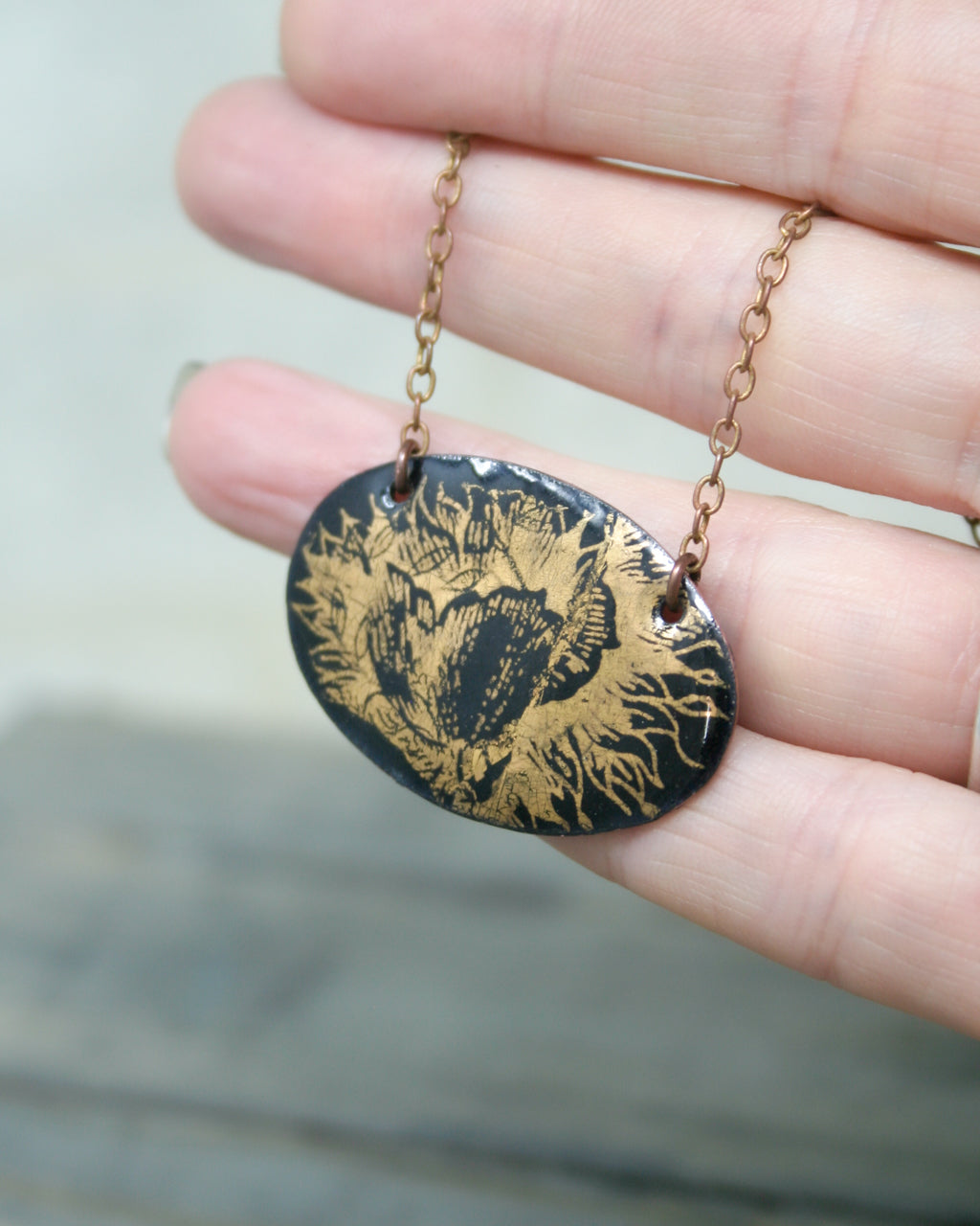 A hand holding a black oval pendant with a gold floral design.