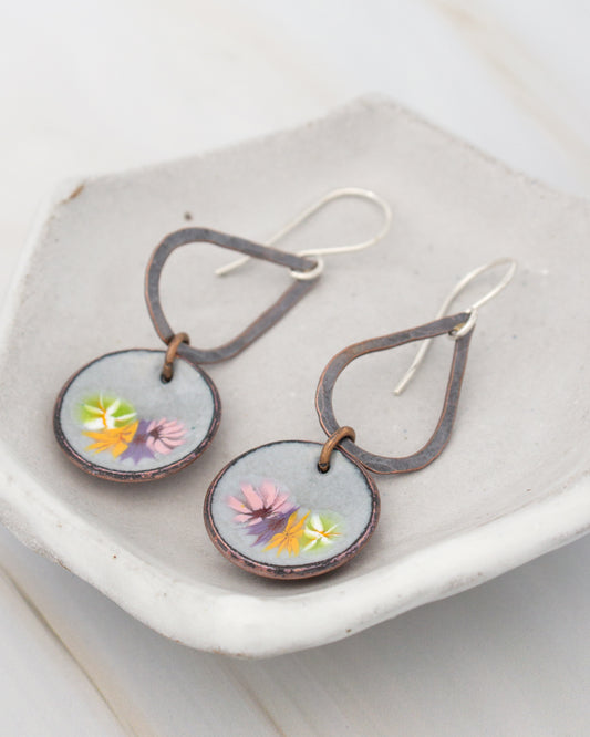 A pair of earrings with a floral design on the circular pendants, displayed on a white surface.