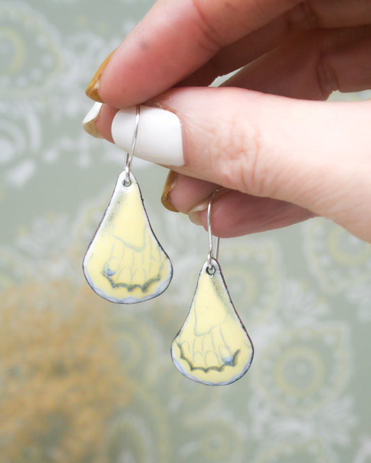 a hand holding a pair of yellow and white earrings