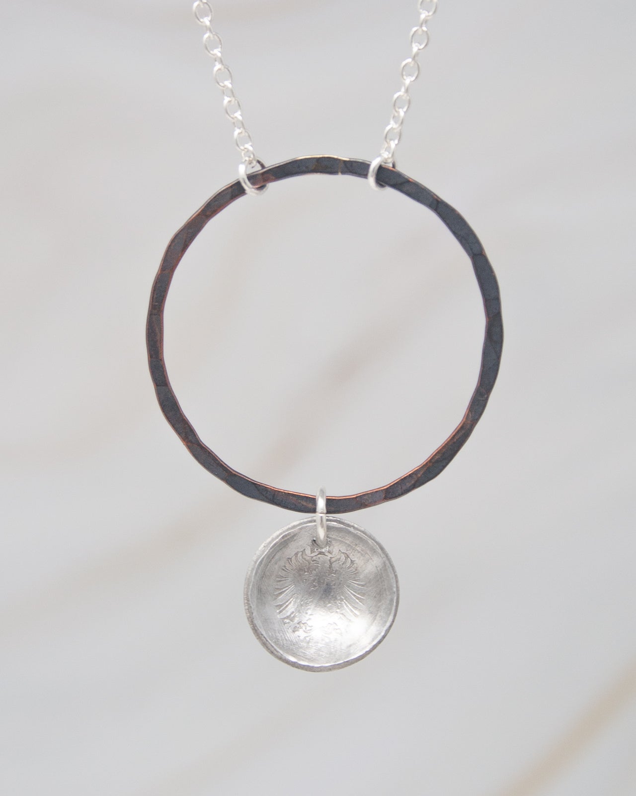 A silver necklace with a circular pendant hanging from a chain.
