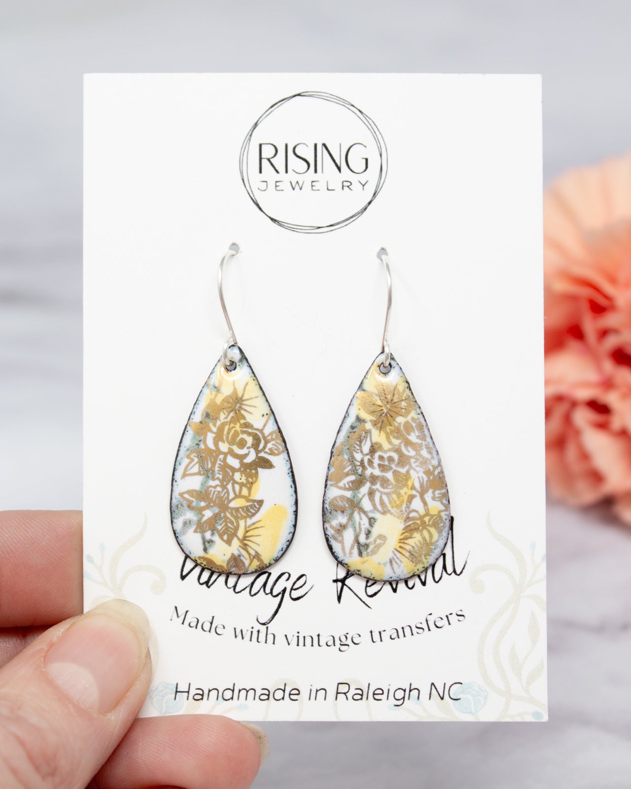 A hand holding a pair of earrings with a floral design, as part of a jewelry product packaging.